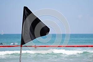 Black flag with a red ribbon on the sea shore warning about dangerous current and waves or invasion of jellyfish