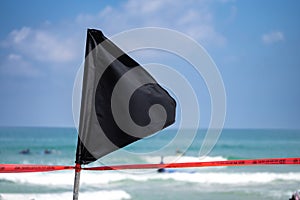 Black flag with a red ribbon on the sea shore warning about dangerous current and waves or invasion of jellyfish.