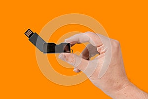 Black flash drive on hand with isolated orange background