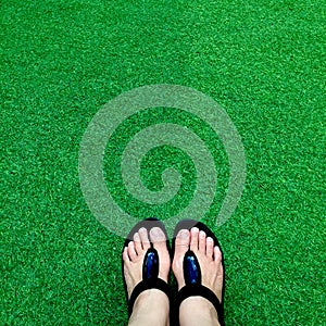 Black flip flops on green lush artificial grass, summer and vacations concept