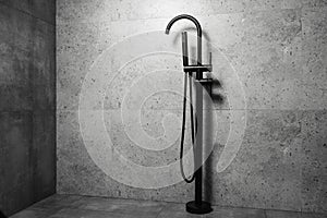 Black floor standing bath taps, on the background of dark grey bathroom walls.