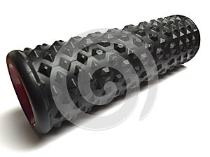 Black foam roller for muscle massage with red interior isolated on white background.  A black bumpy foam massage roller ideal for