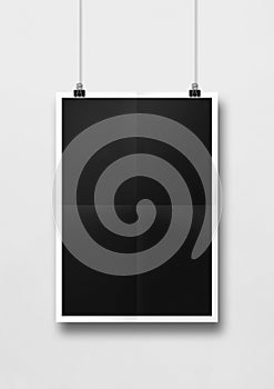 Black folded poster hanging on a white wall with clips