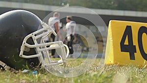 Black football helm lying on pitch, players communicating before important match