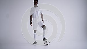 black football player is posing with ball in studio with white background, portrait of forward