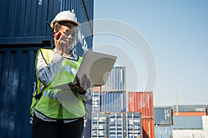 Black foreman woman worker working checking at Container cargo harbor holding laptop computer and walkie-talkie to loading