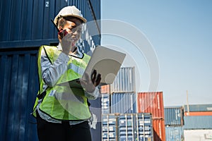 Black foreman woman worker working checking at Container cargo harbor holding laptop computer and walkie-talkie to loading