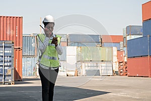 Black foreman woman worker working checking at Container cargo harbor holding radio walkie-talkie and smartphone to loading