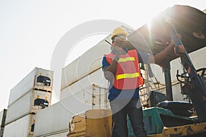 Black foreman worker working control the crane and forklift at Container cargo harbor to loading containers. African dock male