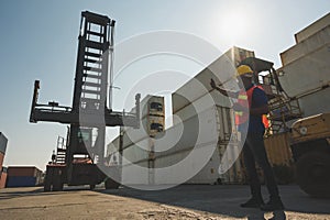 Black foreman worker working control the crane and forklift at Container cargo harbor to loading containers. African dock male