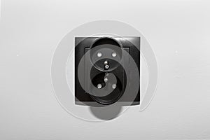 Black frame of a double electrical socket with grounding on the gray wall of the room.