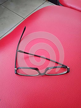 Black frame glasses lay on a red leather chair