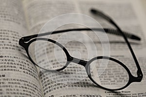 Black frame glasses are placed on the Chinese-English Bible