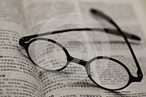 Black frame glasses are placed on the Chinese-English Bible photo