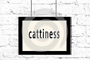 Black frame hanging on white brick wall with inscription cattiness
