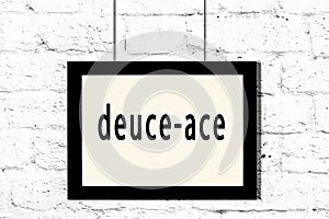 Black frame hanging on white brick wall with inscription deuce-ace photo