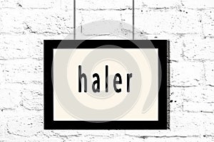 Black frame hanging on white brick wall with inscription haler