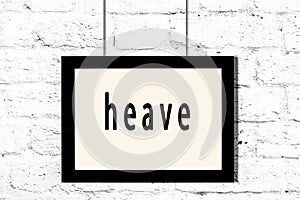 Black frame hanging on white brick wall with inscription heave