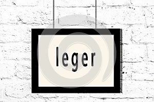 Black frame hanging on white brick wall with inscription leger