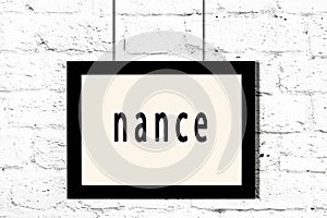 Black frame hanging on white brick wall with inscription nance
