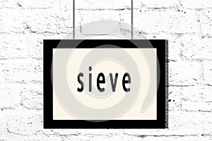 Black frame hanging on white brick wall with inscription sieve
