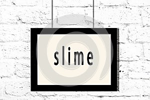 Black frame hanging on white brick wall with inscription slime