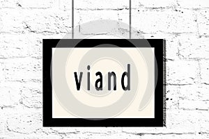 Black frame hanging on white brick wall with inscription viand