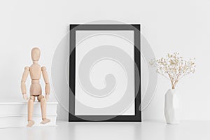 Black frame mockup with books, manikin and a gypsophila in a vase on a white table.Portrait orientation