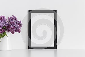 Black frame mockup with a bouquet of lilac in a vase on a white table.Portrait orientation