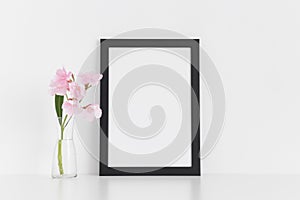 Black frame mockup with pink oleander in a glass vase on a white table.Portrait orientation