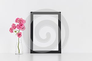 Black frame mockup with pink roses in a glass vase on a white table.Portrait orientation