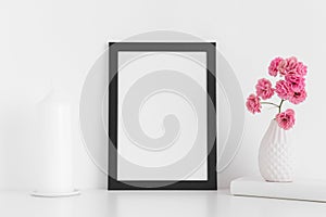 Black frame mockup with pink roses in a vase and candle on a white table.Portrait orientation