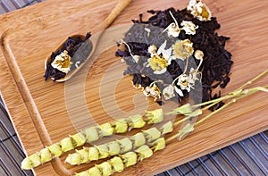 Black friable tea with sage and chamomile. On wooden spoon on tr