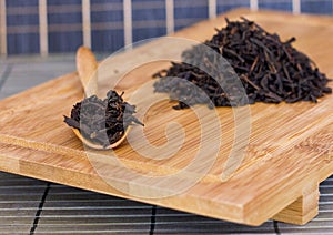 Black friable tea in a wooden spoon and on a wooden tray