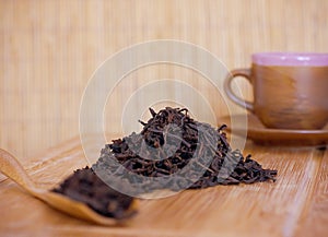 Black friable tea in a wooden spoon and on a wooden tray