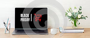 Black friday concept. Laptop computer screen with shopping card and sign `Black friday` on wooden desk