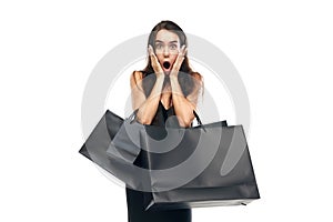 Black friday concept. Portrait of shocked woman wearing black dress raising hands with bags. Beginning season of sales.
