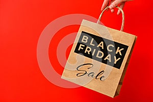 Black Friday, female hand holding brown craft shopping bag isolated on red background. Black friday sale, discount