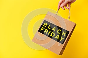 Black Friday, female hand holding brown craft shopping bag on yellow background. Black friday sale, discount, recycling