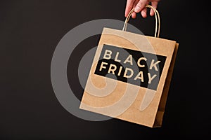 Black Friday, female hand holding craft shopping bag isolated on black background. Black friday sale, discount