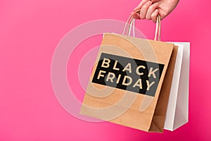 Black Friday, female hand holding two shopping bags isolated on pink background. Black friday sale, discount, shopping