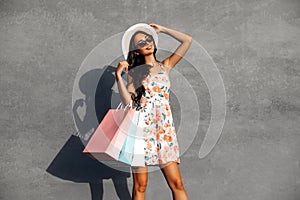 Black Friday, Happy beautiful young woman in black sunglasses with shopping bags, outdoors on gray city wall background