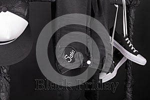 Black friday. Sale sign. and white snaekers, cap pant, jeans hanging on clothes rack background. Close up.