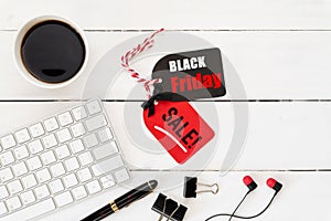 Black Friday Sale text on a red and black tag with coffee cup and Earphone on white wooden table background. Shopping
