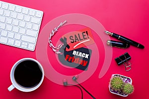 Black Friday Sale text on a red and black tag with coffee cup, plant table, gift box Earphone and mouse keyboard on red background