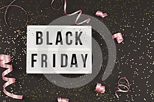 Black friday sale text on white lightbox, golden stars and holiday ribbon around on black background