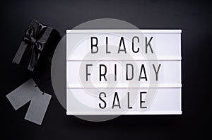 Black Friday Sale words on lightbox with black giftbox and price tags top view flat lay on black background