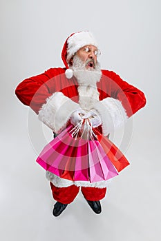 Full-length portrait of senior man wearing Santa Claus costume, holding many shopping packages isolated over white