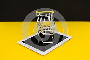 Black Friday sales. Small shopping trolley on a tablet in yellow background. Cybermonday concept
