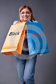Black Friday, Shopping and commerce concept. Sake and discount. Woman with bags standing on a gray background.